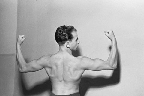 Archival portrait of a boxer flexing his arms, photographed from behind
